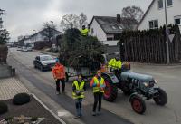 Pfadfinder in Warnwesten stehen vor einem Traktor mit Hänger, der Christbäume geladen hat.