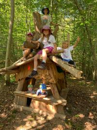 Kinder sitzen im Wald auf einer kleinen Holzhütte.